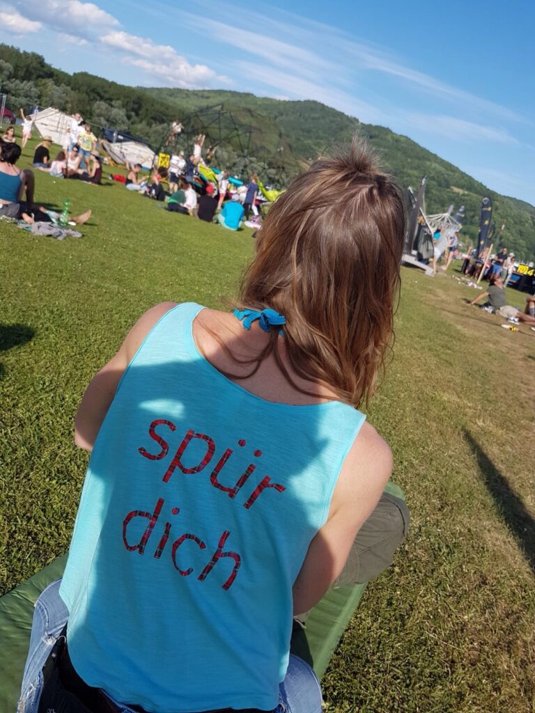 Doris Sattelberger mit „spür dich“-Shirt sitzt auf einer Wiese bei einer Veranstaltung im Freien