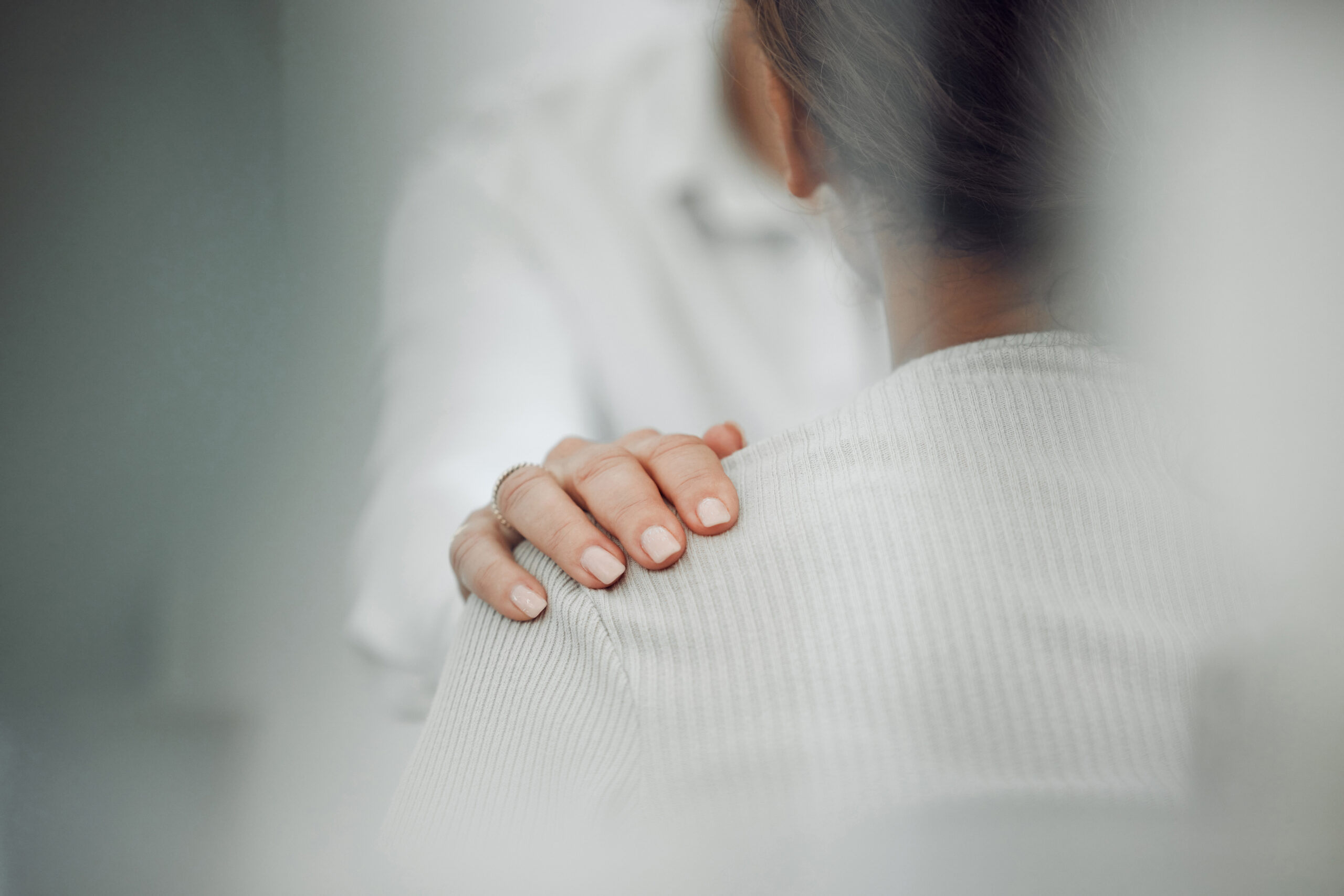 Hand liegt sanft auf der Schulter einer sitzenden Person