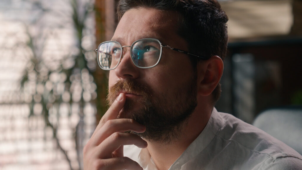 Nachdenklicher Mann mit Brille blickt nach oben und berührt sein Kinn